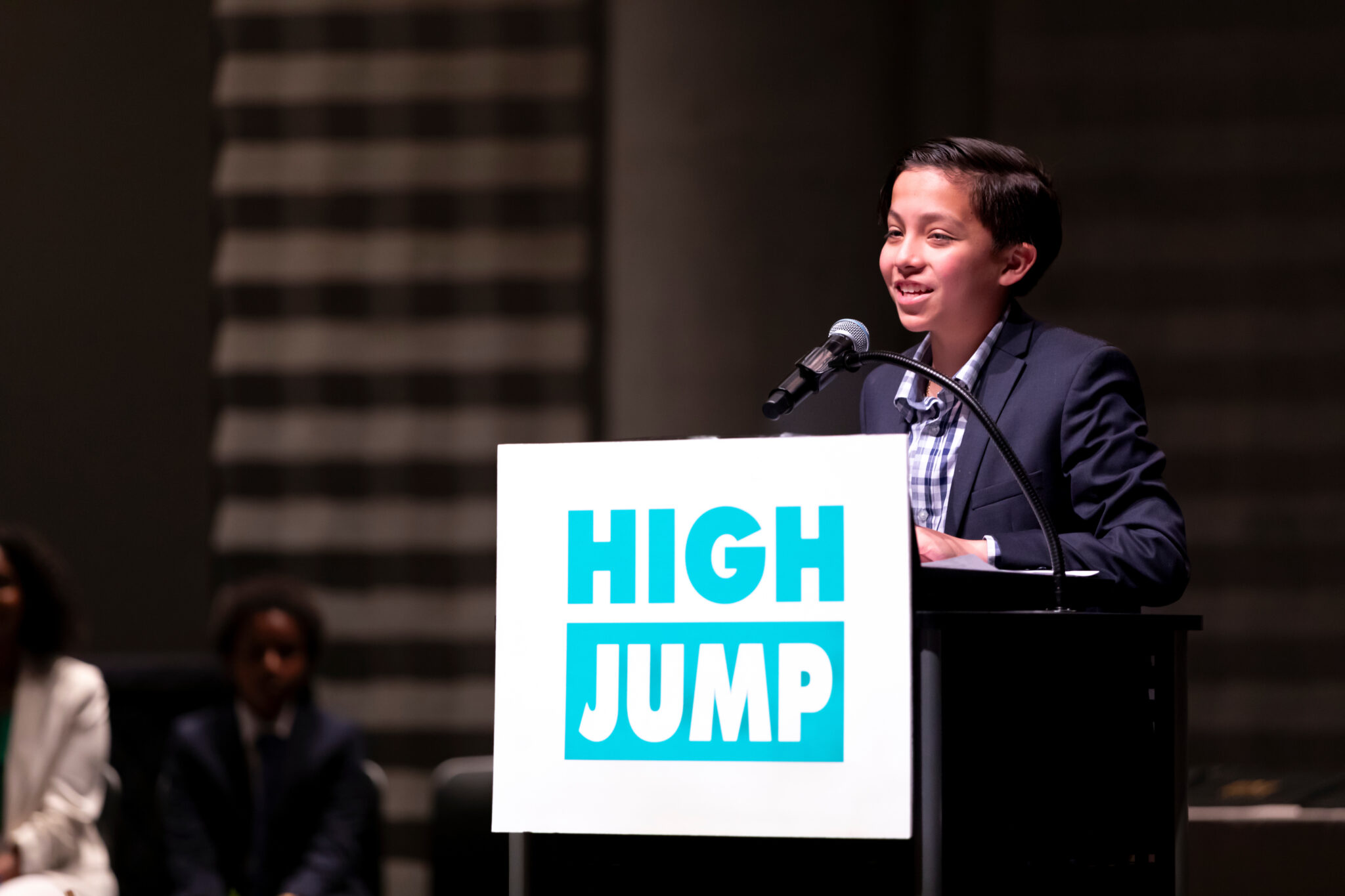 Leo stands at a High Jump podium with a microphone and speaks