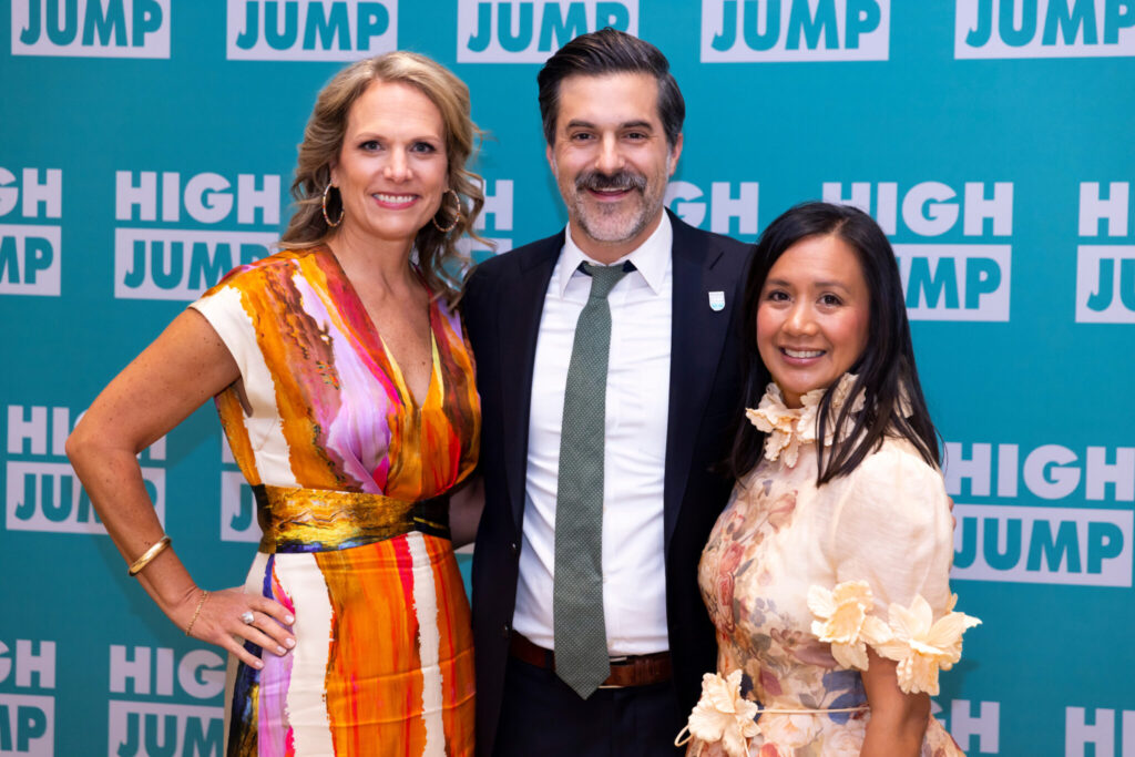 Cindy O'Connor (High Jump board chair), Nate Pietrini (Executive Director), and Lena Jessen (High Jump board chair elect) stand in front of a High Jump step and repeat at the 2024 Spring of Opportunity Benefit